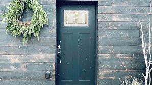 A dark wooden door with a wreath on the wall to the left and a small step leading up to it.
