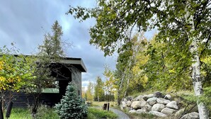 A pathway leading to a rustic cabin with a wooden exterior, surrounded by trees and a stone wall.