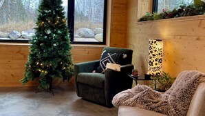 A cozy room with a Christmas tree, a green armchair, a fluffy throw, and a lamp on a side table.