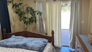 A bedroom with a bed, a dresser, a plant, and a window with curtains. - Quiet Country 1-bedroom apartment in Royal Oaks with beautiful views (Prunedale)