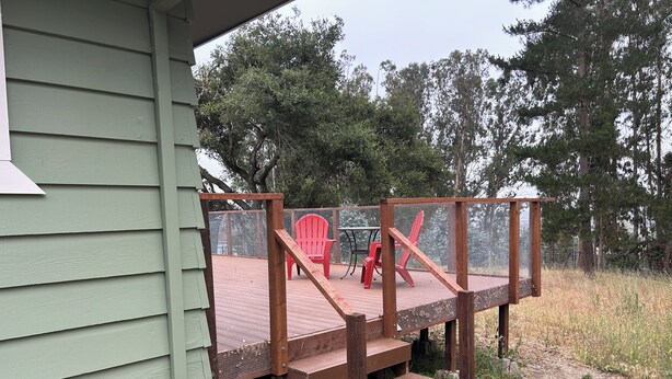A wooden deck with a mesh enclosure, a red Adirondack chair, and a table. - Quiet Country 1-bedroom apartment in Royal Oaks with beautiful views (Prunedale)