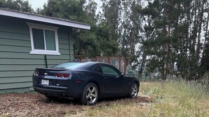 A car parked in a grassy area with a house in the background. - Quiet Country 1-bedroom apartment in Royal Oaks with beautiful views (Prunedale)