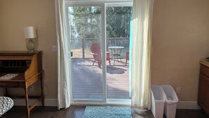 A room with a wooden desk, a lamp, a sliding glass door leading to an outdoor patio with a table and chairs. - Quiet Country 1-bedroom apartment in Royal Oaks with beautiful views (Prunedale)