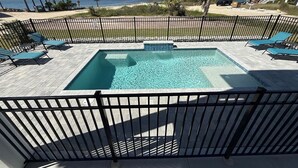 A rectangular pool with a black metal fence, surrounded by lounge chairs and a view of the ocean. - New! Bayfront home w/ Pool, Golf Cart, Kayaks, Bikes & The Islands Best Sunsets! (Saint George Island)