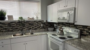 A kitchen with white cabinets, a granite countertop, a stove, and a microwave. - Charming Room 6 in the St. Maries Inn (Saint Maries)