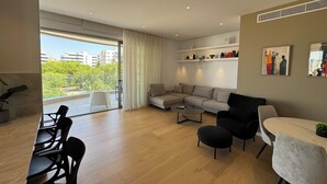 Ein modernes Wohnzimmer mit Sofa, Stühlen, einem Esstisch und einem Balkon mit Blick auf Gebäude und Bäume.