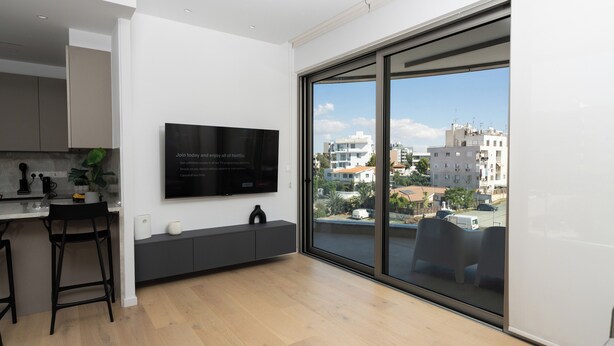 Eine moderne Küche mit großem Fernseher, Holzboden und Blick auf die Stadt durch große Fenster.