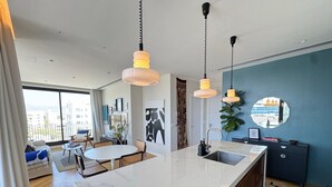A modern kitchen with a marble countertop, pendant lights, and a view of the city through large windows.