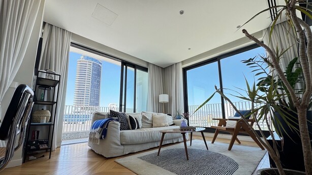A modern living room with a large sofa, a coffee table, and a view of a cityscape through large windows.