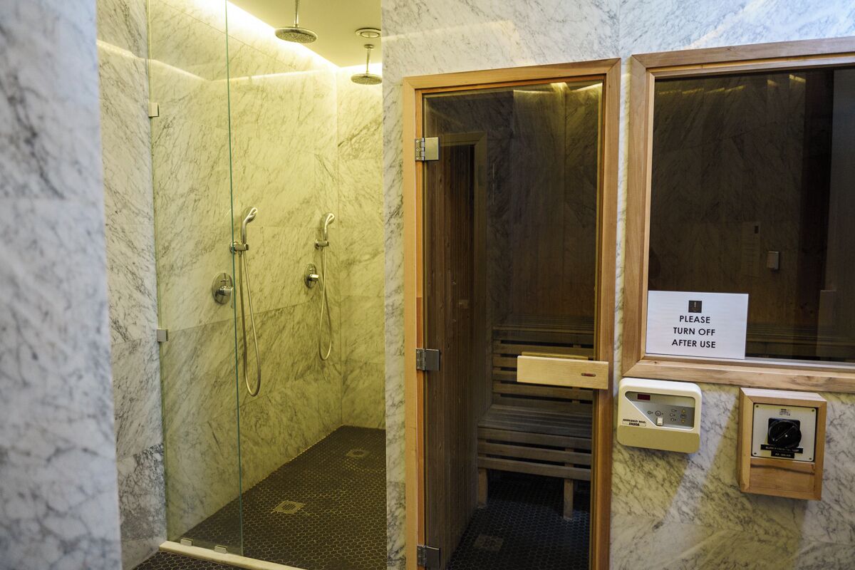 A modern bathroom with a glass-enclosed shower, marble walls, and a wooden door.