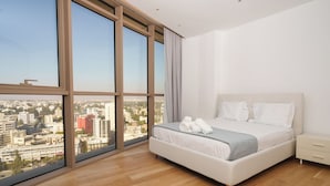 Un dormitorio moderno con un ventanal grande, una cama con ropa de cama blanca y una mesita de noche.