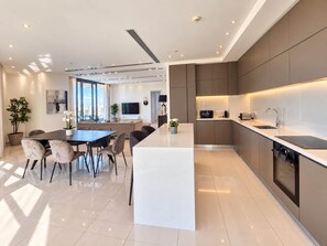 Een moderne keuken met een centraal kookeiland, inbouwapparatuur en een eethoek met een grote tafel en stoelen.