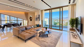 A modern living room with a large sofa, a dining area with chairs, a coffee table, and a TV on a stand.
