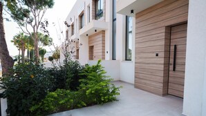 A modern building with a wooden facade, a gated entrance, and a landscaped garden area. - WealthyStays 2BR Retreat | 5Min Walk to Beach (Protaras)