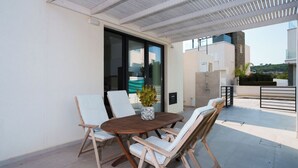 A covered outdoor seating area with a round wooden table and four white cushioned chairs. - WealthyStays 2BR Retreat | 5Min Walk to Beach (Protaras)