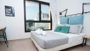 A bedroom with a bed, a desk, a chair, a window, and a wall sign. - WealthyStays 2BR Retreat | 5Min Walk to Beach (Protaras)