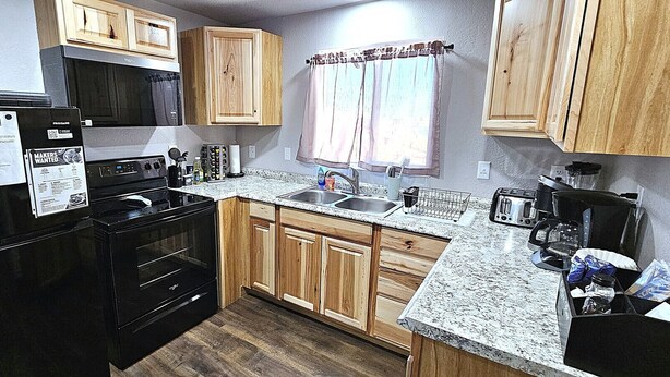 Una cocina compacta con armarios de madera, una estufa negra, un lavamanos y un ventanal con cortinas.
