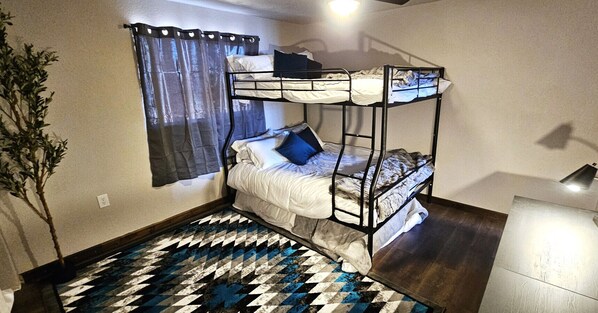 A bunk bed room with a patterned rug, a potted plant, and a window with curtains.