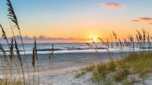 A beach scene with sand, grass, and the ocean.