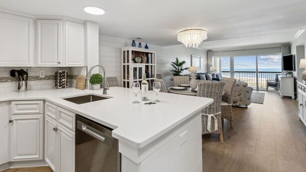 A modern kitchen with white cabinetry, a central island, and a dining area with wicker furniture.