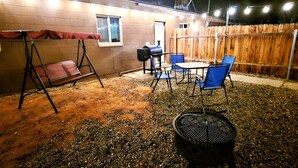 Un espace extérieur aménagé en patio, avec une balançoire, un barbecue et des chaises bleues.