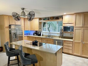 Una cocina moderna con armarios de madera, electrodomésticos de acero inoxidable, una isla central con asientos y un amplio ventanal con vistas al exterior.