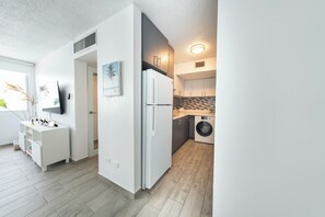 A modern kitchen with a built-in washing machine, white cabinetry, and a small dining area with a white table and chairs. - Beachfront Wave at Isla Verde (Carolina)