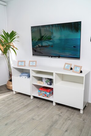 A white entertainment unit with two framed certificates, a large TV, and a potted plant. - Beachfront Wave at Isla Verde (Carolina)