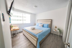 A bedroom with a bed, a desk, a window, and a small table with a plant. - Beachfront Wave at Isla Verde (Carolina)