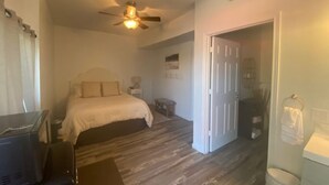 A bedroom with a bed, a ceiling fan, a nightstand, a small table, and a door leading to another room. - Charming Room 7 in the St. Maries Inn (Saint Maries)