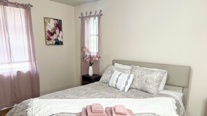 Ein ordentlich gemachtes Bett mit einer gemusterten Tagesdecke, Kissen und einem Stapel rosa Handtücher.