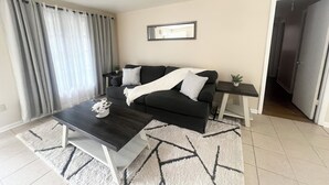 Ein modernes Wohnzimmer mit einem dunklen Sofa, weißen Kissen, einem Couchtisch und einem Teppich.