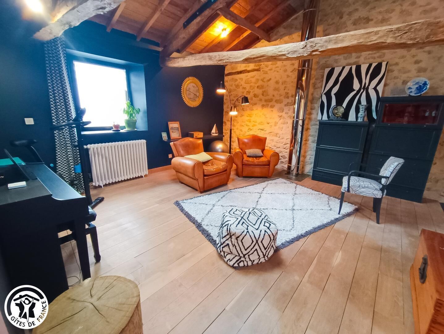 A cozy living room with a large window, two leather armchairs, a patterned rug, and a wooden ceiling.