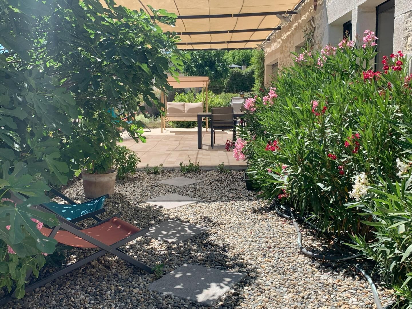 A patio area with a table and chairs, surrounded by potted plants and flowering shrubs.