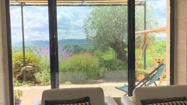 A room with two beige sofas, one with a striped pillow and the other with a polka-dotted pillow, facing a large window with a view of a garden and a swing set.
