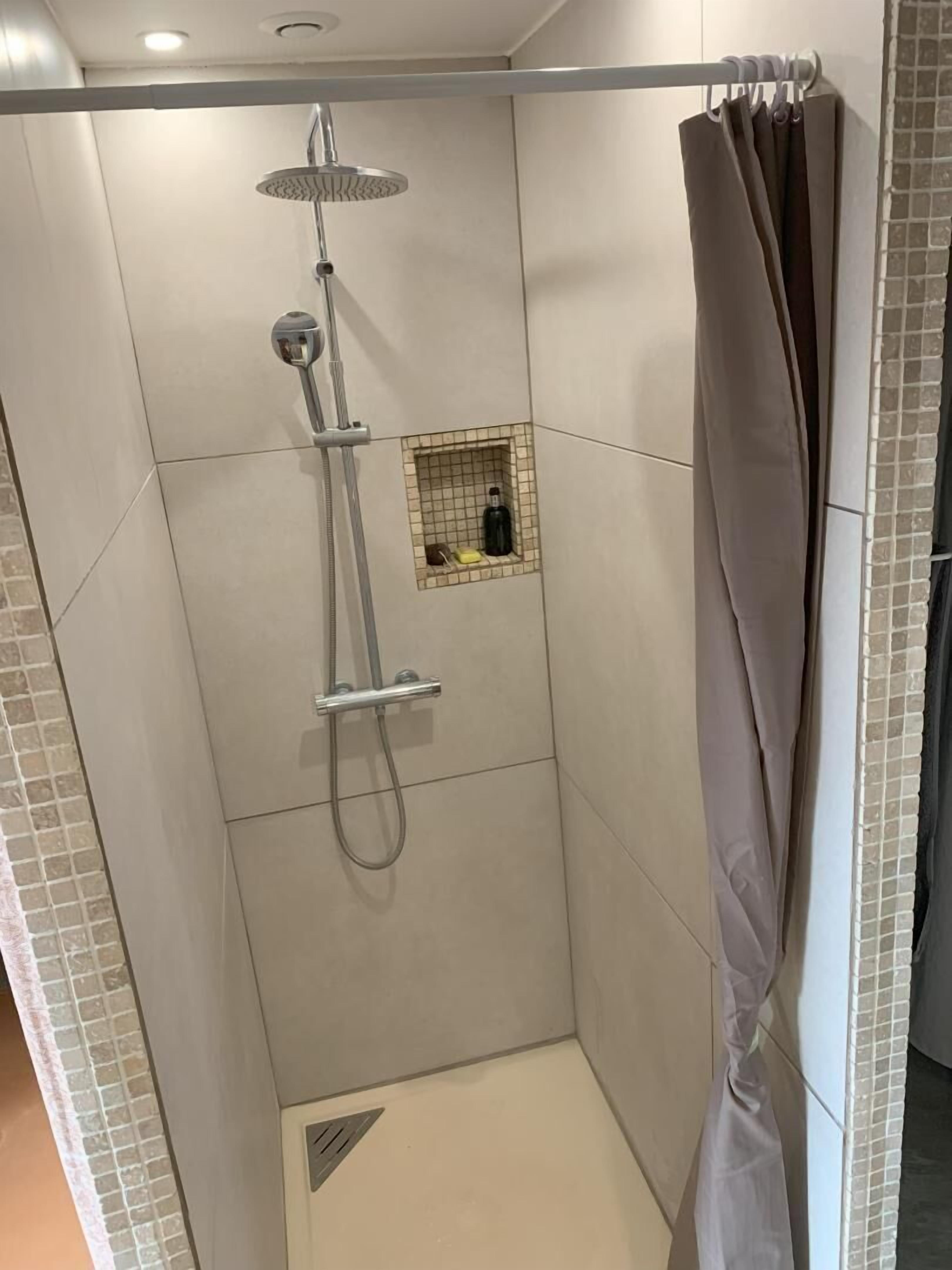 A shower area with a showerhead, a handheld shower, and a small shelf with toiletries.