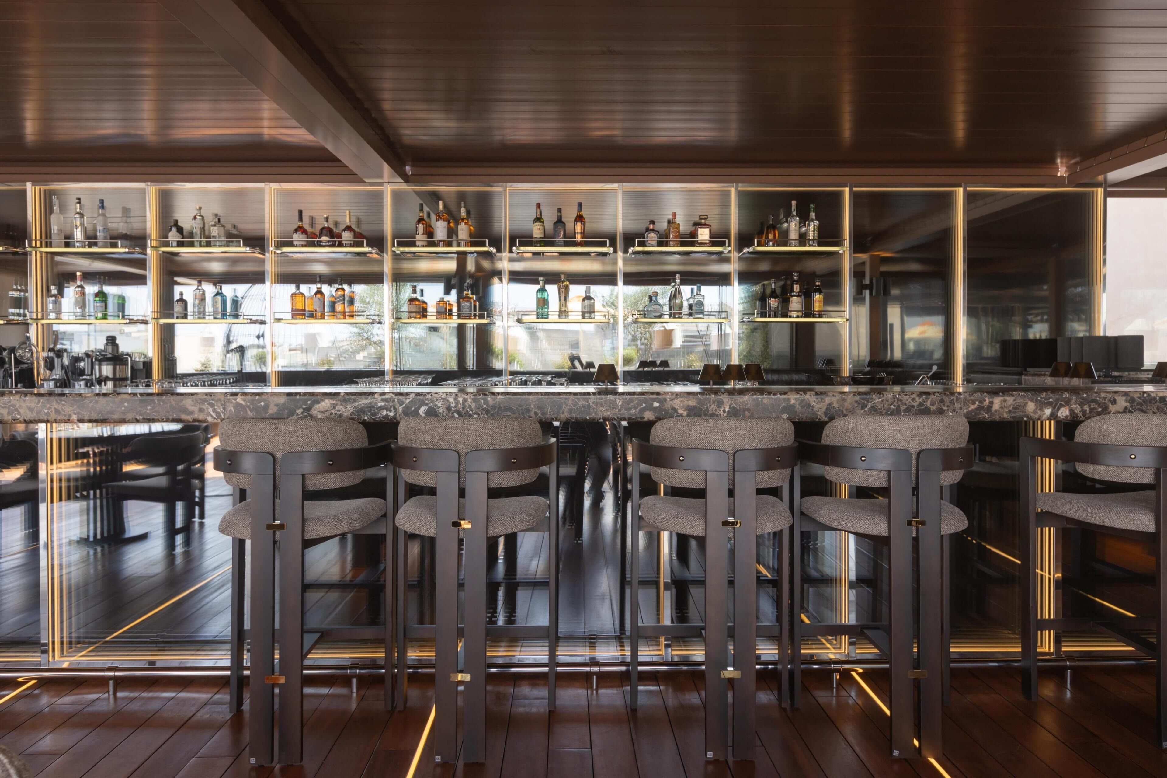 A bar area with multiple stools and shelves stocked with bottles.