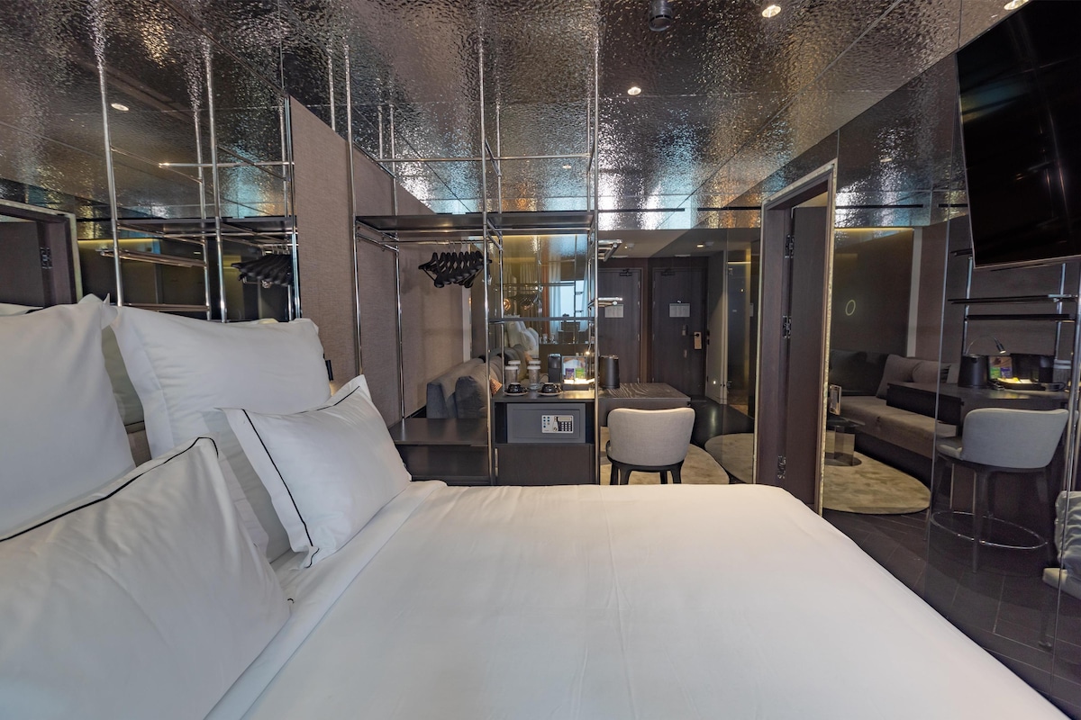 Habitación de hotel moderna con una cama grande, un escritorio con computadora y una zona de estar con sofá y sillones.