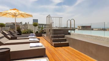 A rooftop terrace with sun loungers, a pool, and a view of the city.