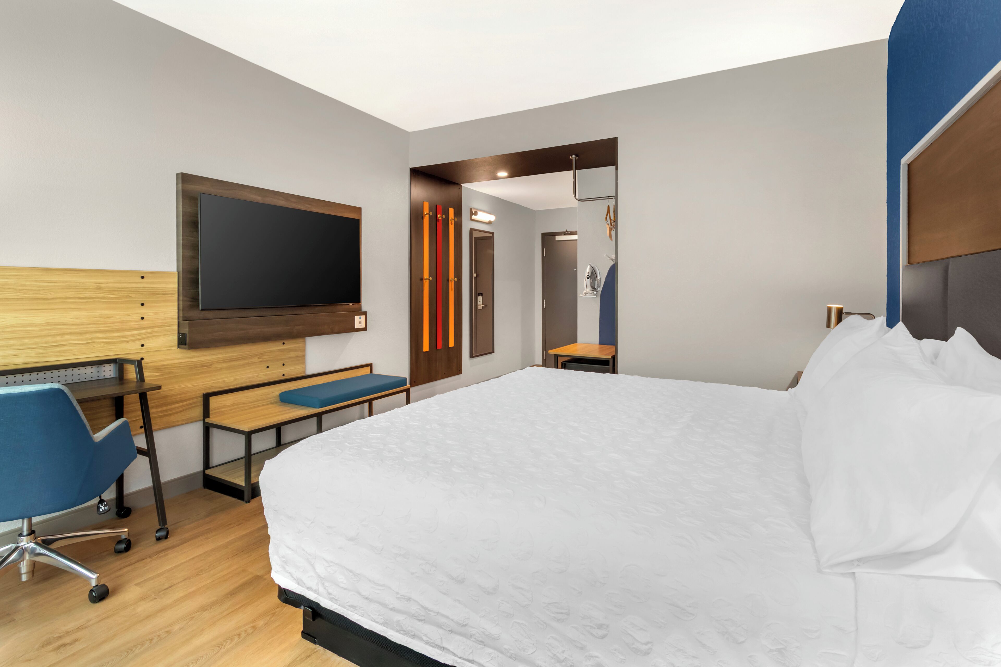 Una habitación de hotel moderna con una cama grande, un escritorio con silla, un televisor de pantalla plana montado en la pared y un espejo.