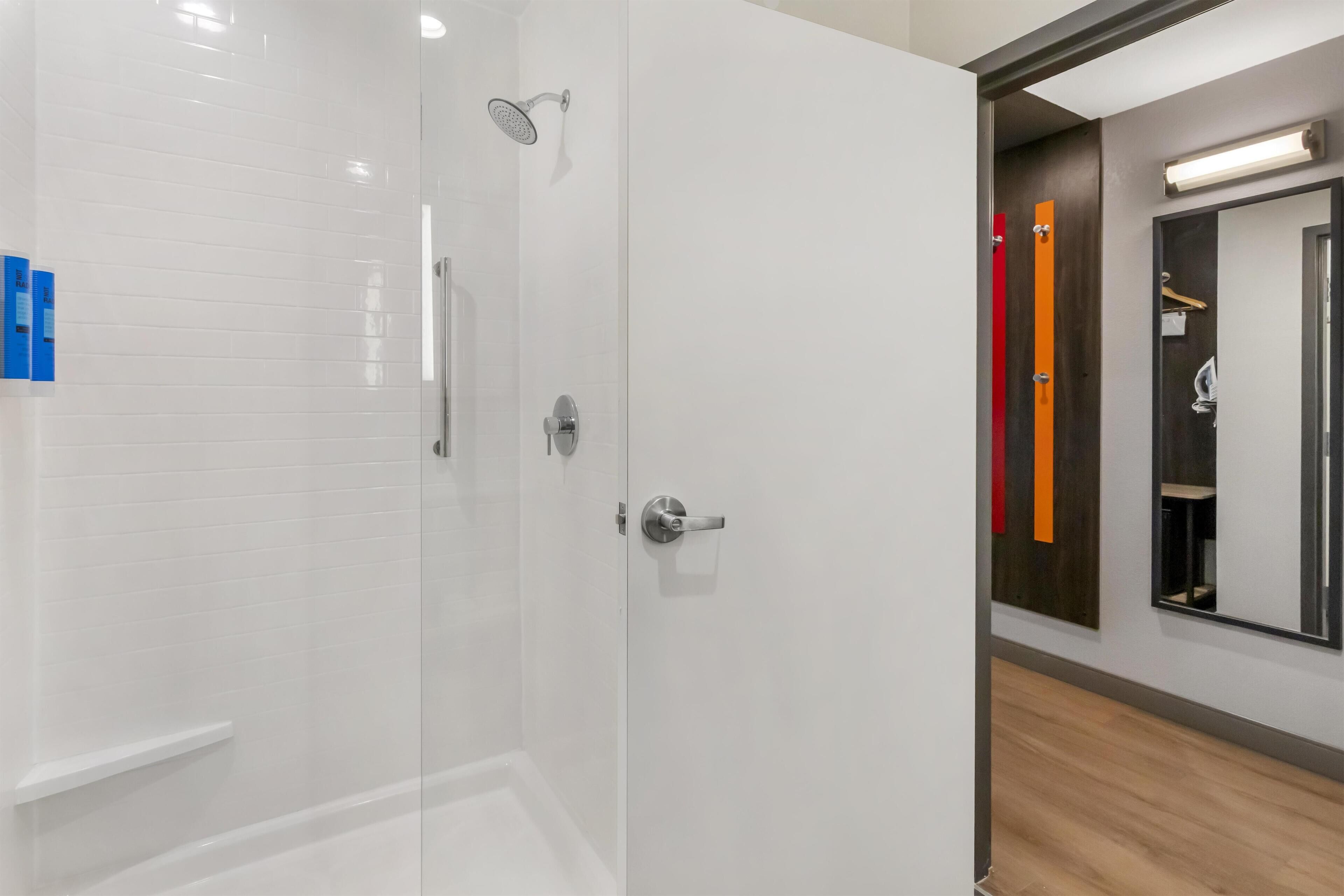 Un baño moderno con ducha de vidrio, pared de azulejos blancos y piso de madera.