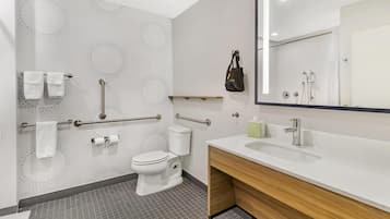 A modern bathroom with a toilet, grab bars, a sink, and a mirror.