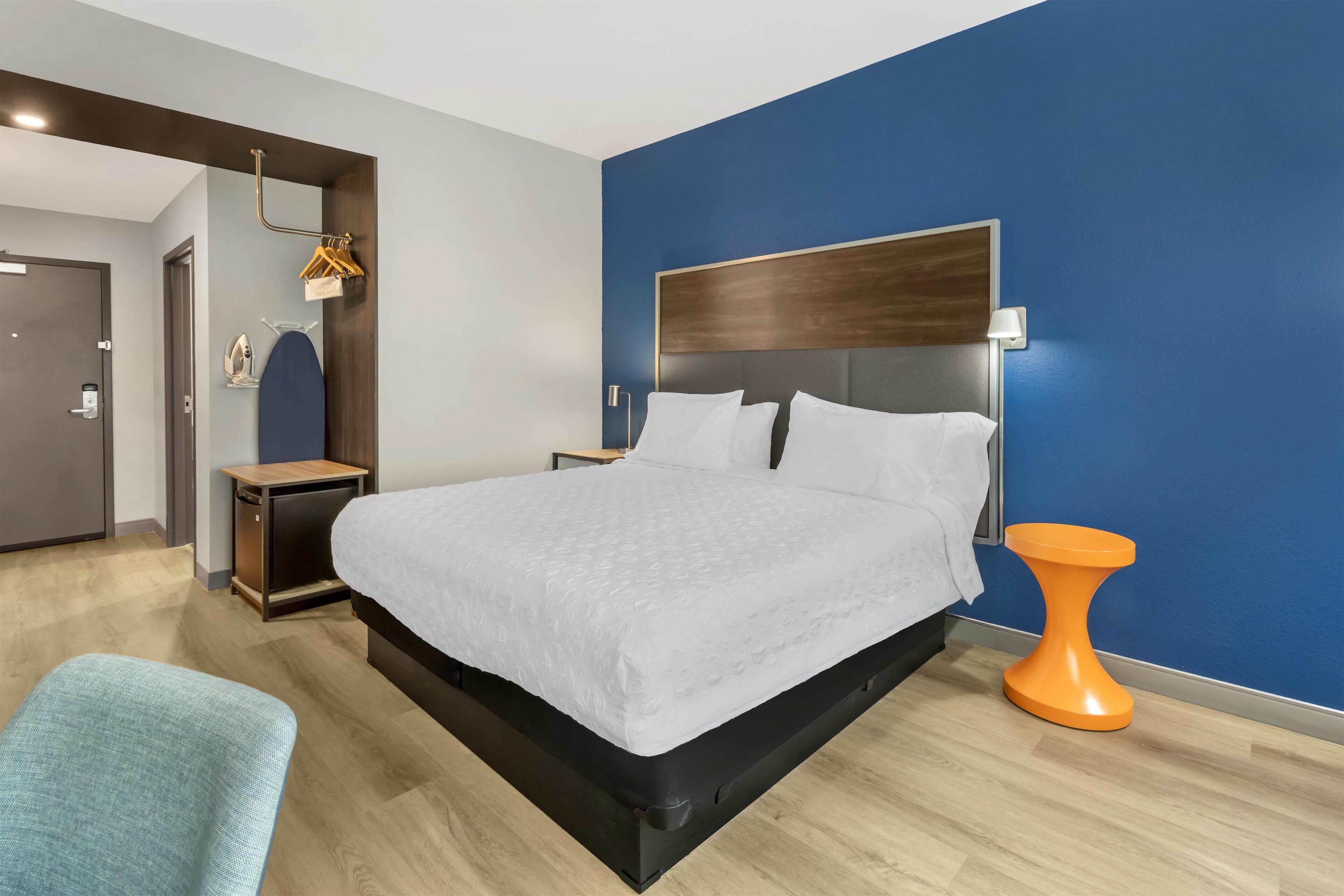 Une chambre d’hôtel moderne, dotée d’un grand lit, d’une table de chevet, d’une chaise et d’une table d’appoint orange au design original.