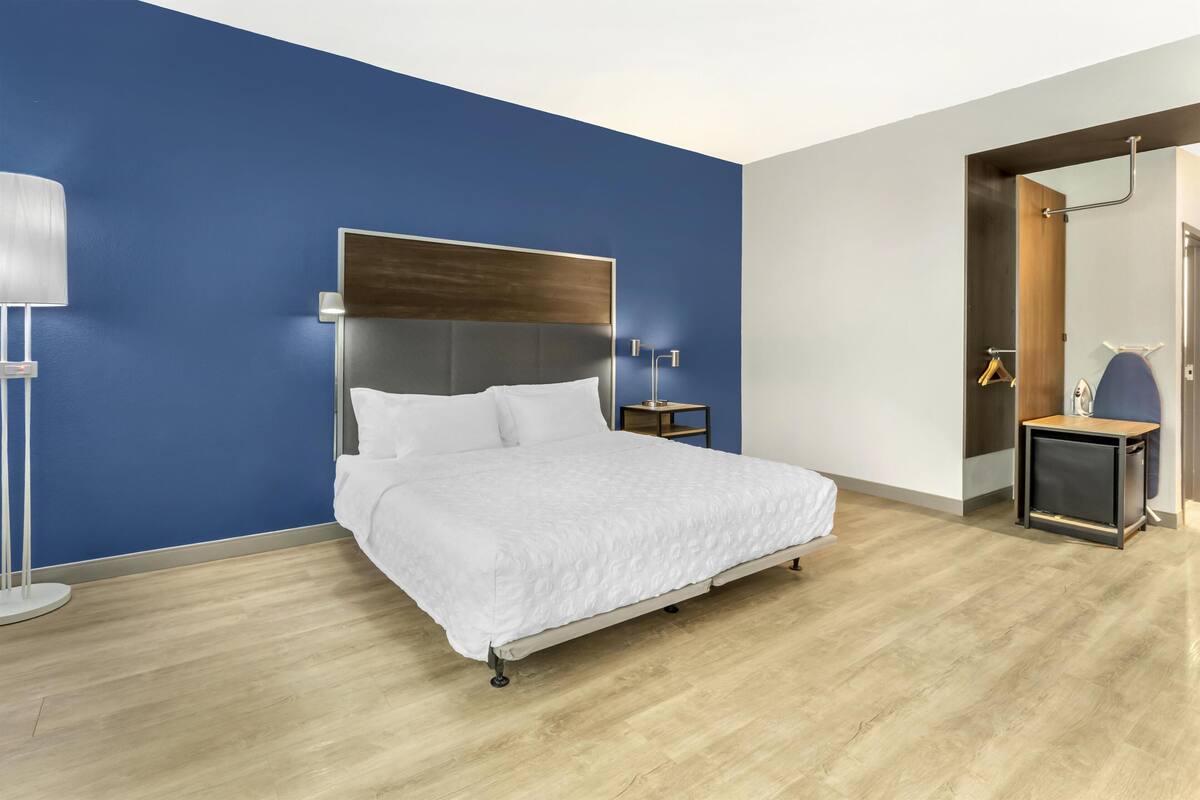 A modern hotel room with a large bed, a bedside table, a floor lamp, and a wardrobe.
