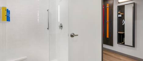 A modern bathroom with a glass-enclosed shower, a white tiled wall, and a wooden floor.