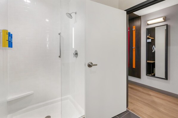 A modern bathroom with a glass-enclosed shower, a white tiled wall, and a wooden floor.