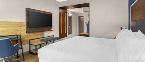 Quarto de hotel moderno com uma cama grande, uma escrivaninha com cadeira, uma televisão de tela plana fixada na parede e um espelho.