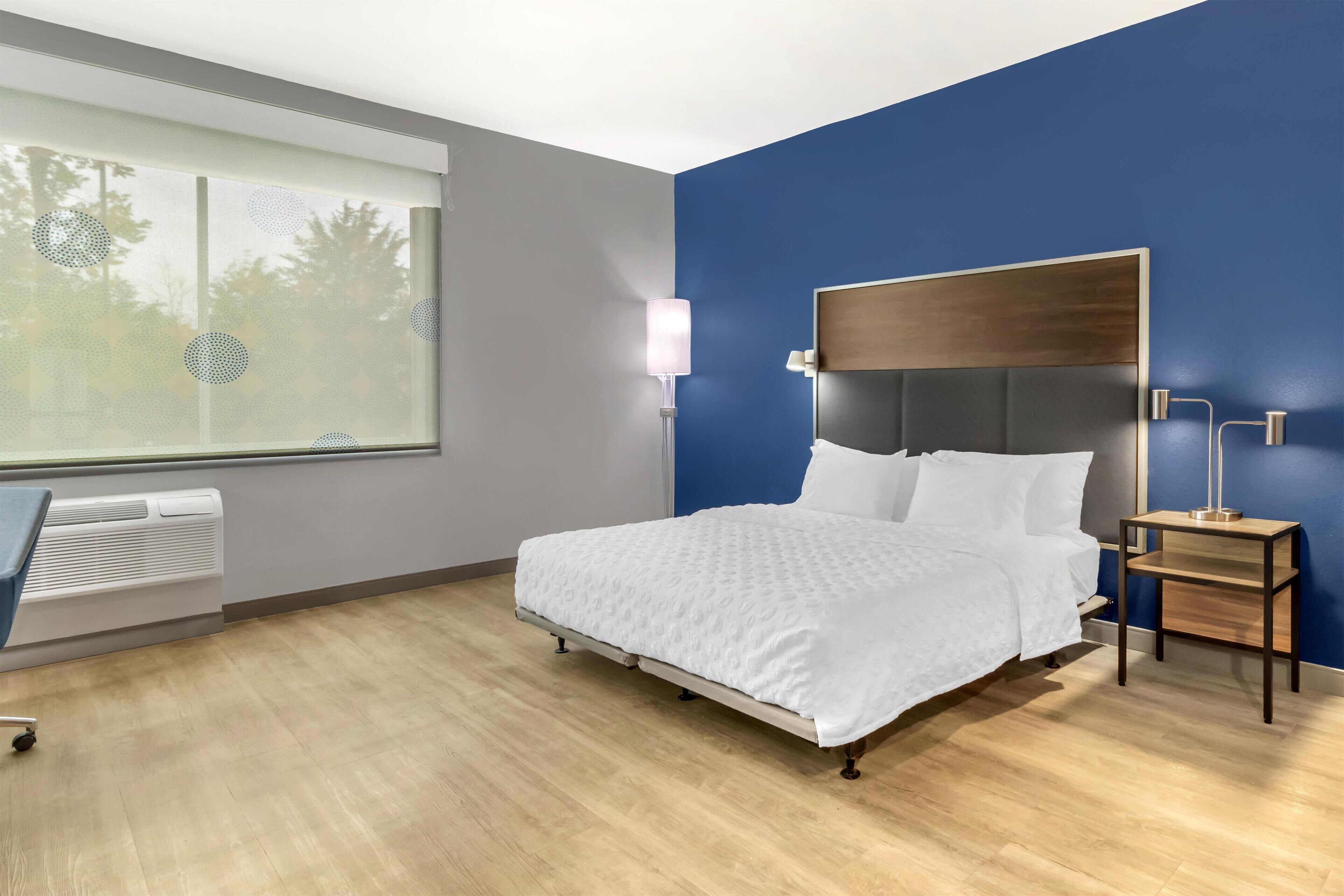 Un dormitorio moderno con cama, mesita de noche, lámpara y un ventanal con persianas.