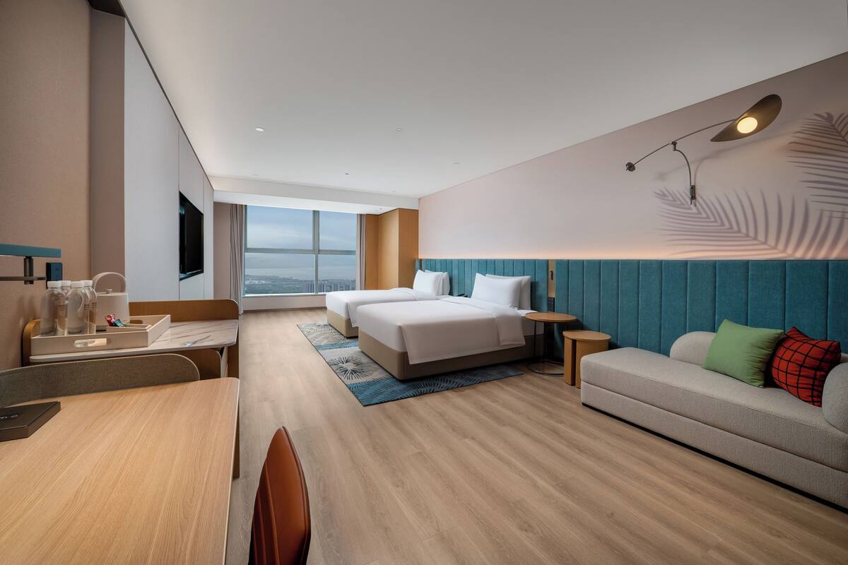 A modern hotel room with a large bed, a sofa, a desk, and a TV.
