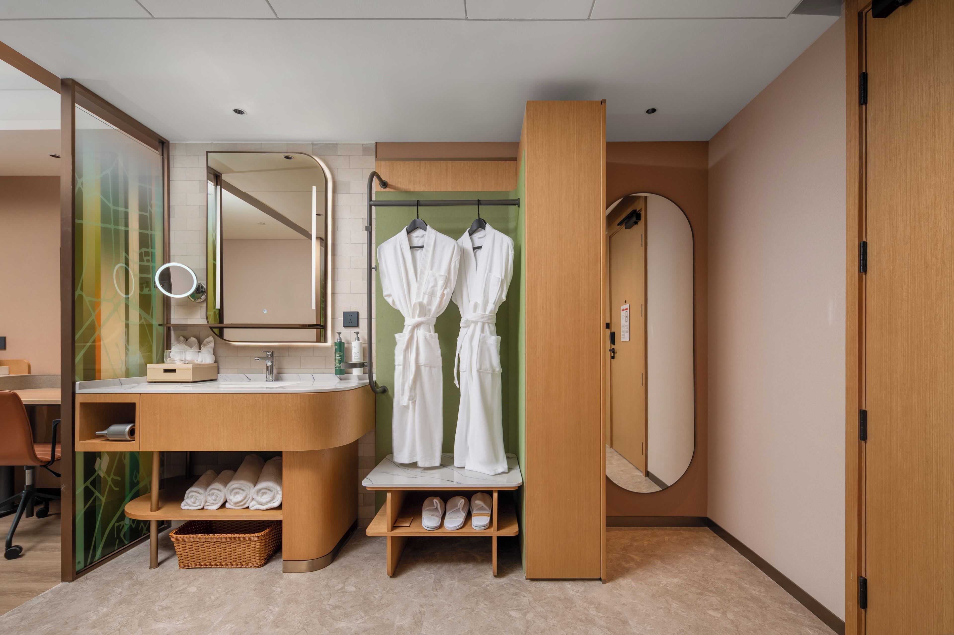 A modern bathroom with a vanity, a mirror, a shower, and two white robes hanging on a rack.